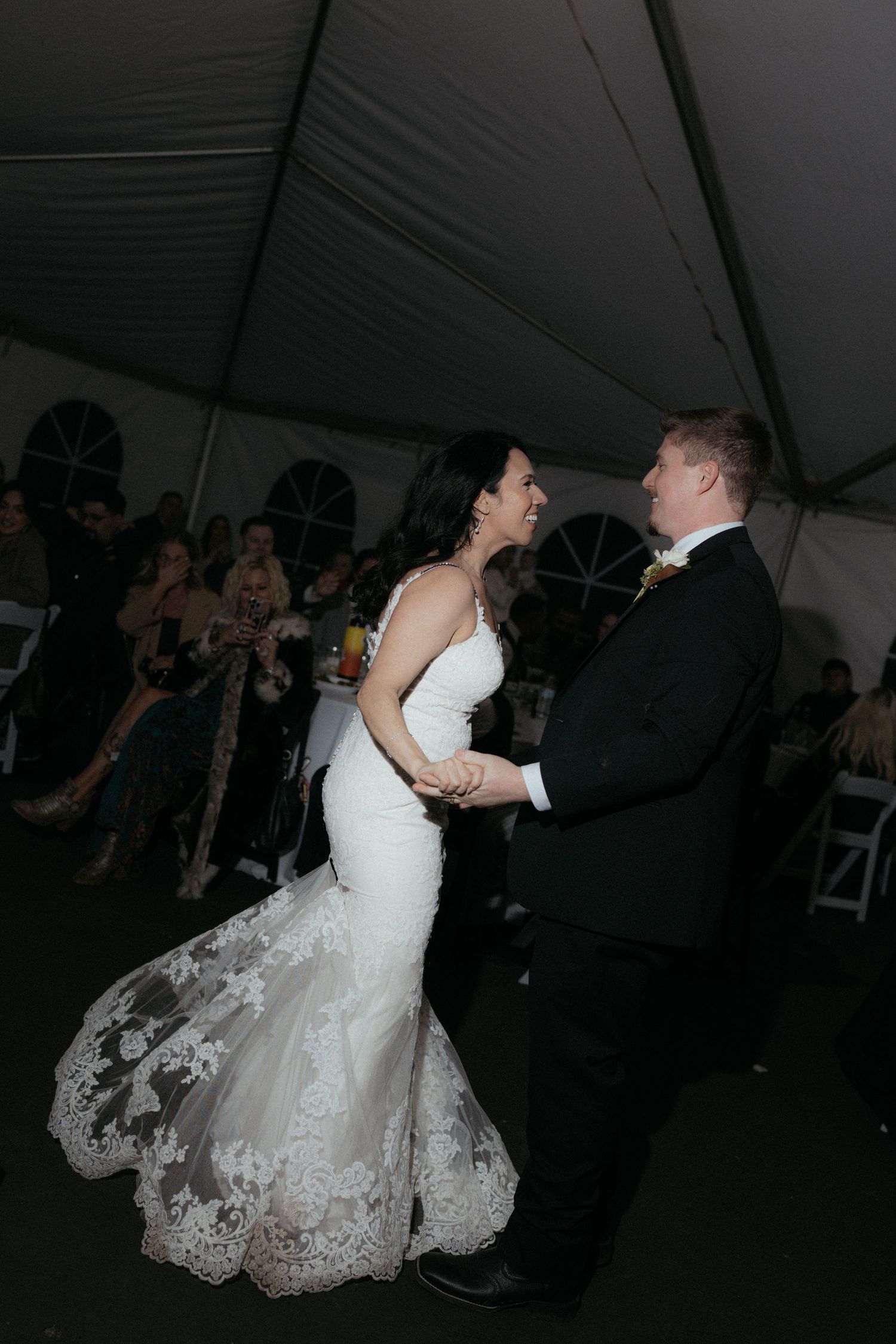 A couple performs a romantic dip dance move during their wedding reception under a white tent.