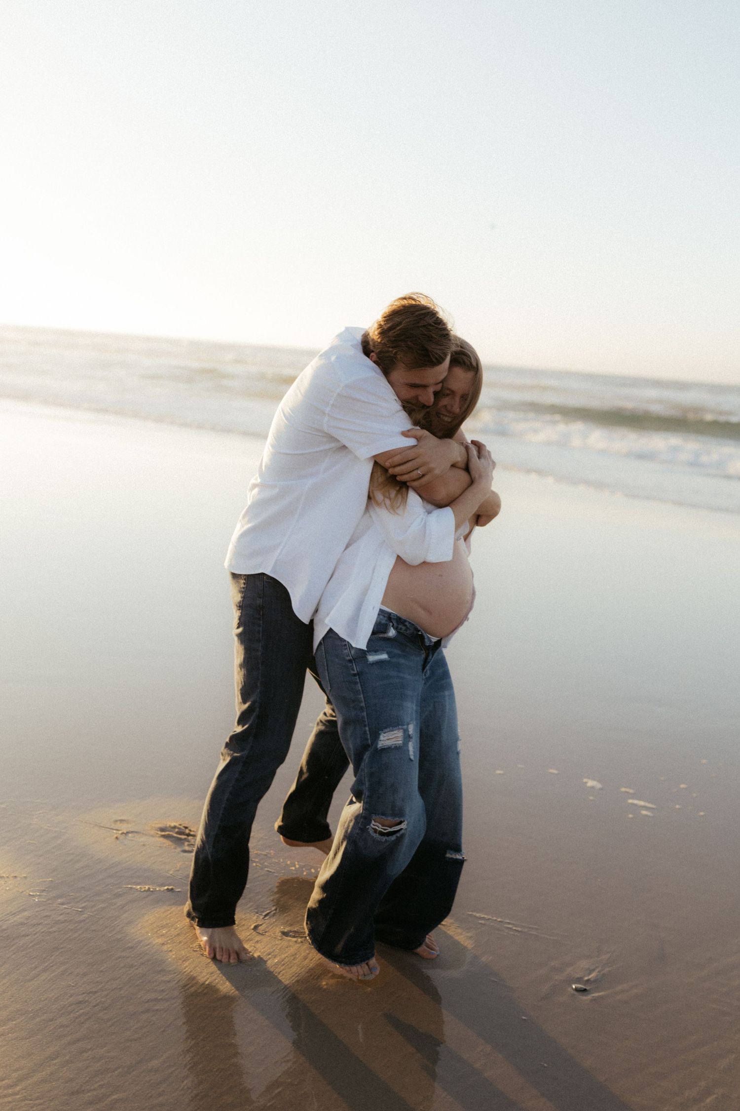 Couple embracing on a sandy beach at sunset with waves in the background.