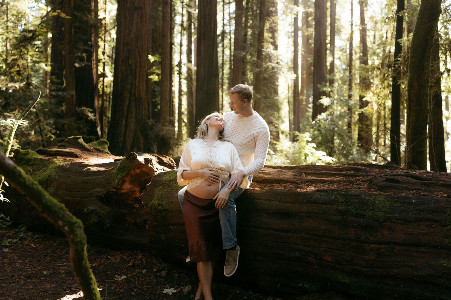 A family enjoys a peaceful moment together while sitting on fallen logs in a sunlit redwood forest.