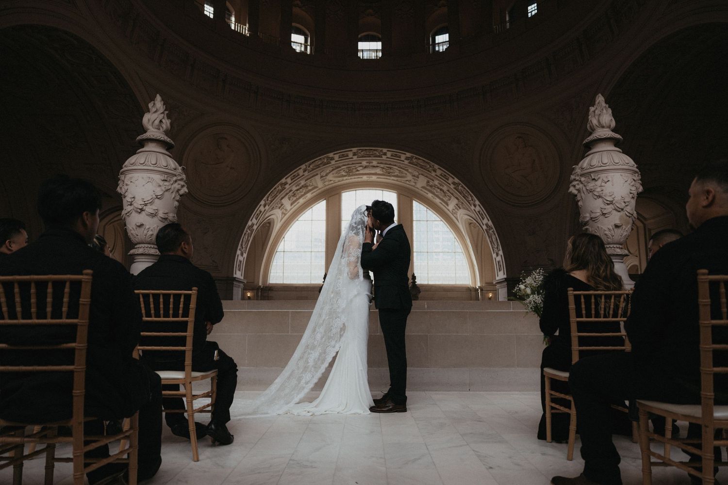 A dramatic wedding ceremony in a dark stone chapel with elegant wooden chairs and soft natural lighting.