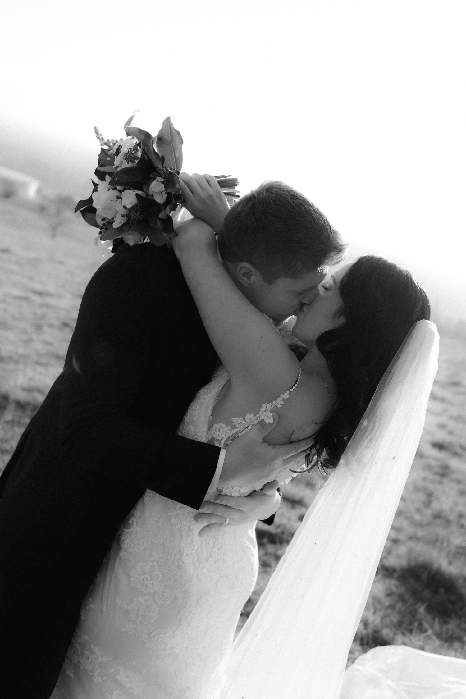 A romantic black and white photo of newlyweds sharing their first kiss as a married couple.