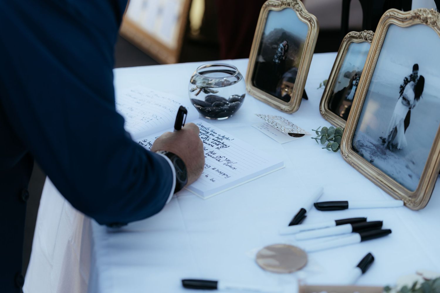 Wedding reception table setup with framed photos and writing materials in blue tones.