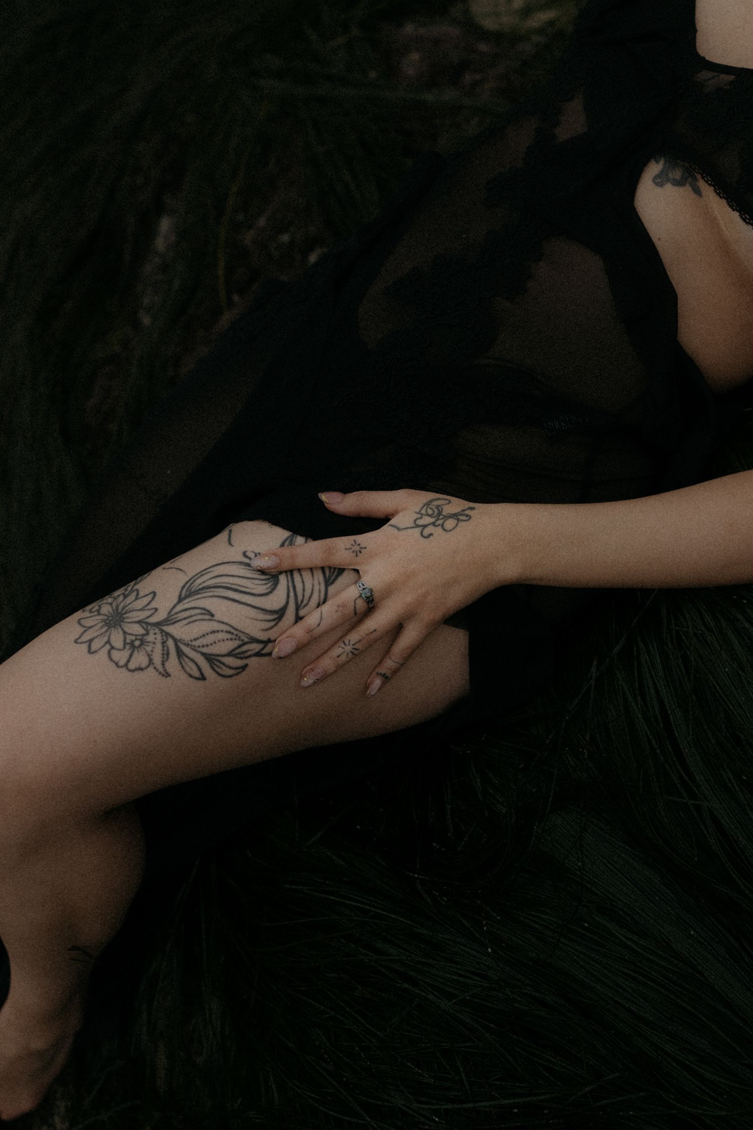 Artistic black and white photo showing tattooed leg with floral design against dark background.