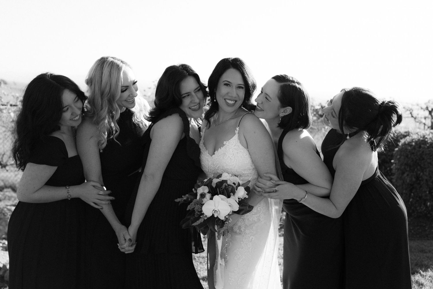 A series of black and white candid wedding photos showing joyful moments and embraces between wedding party members.