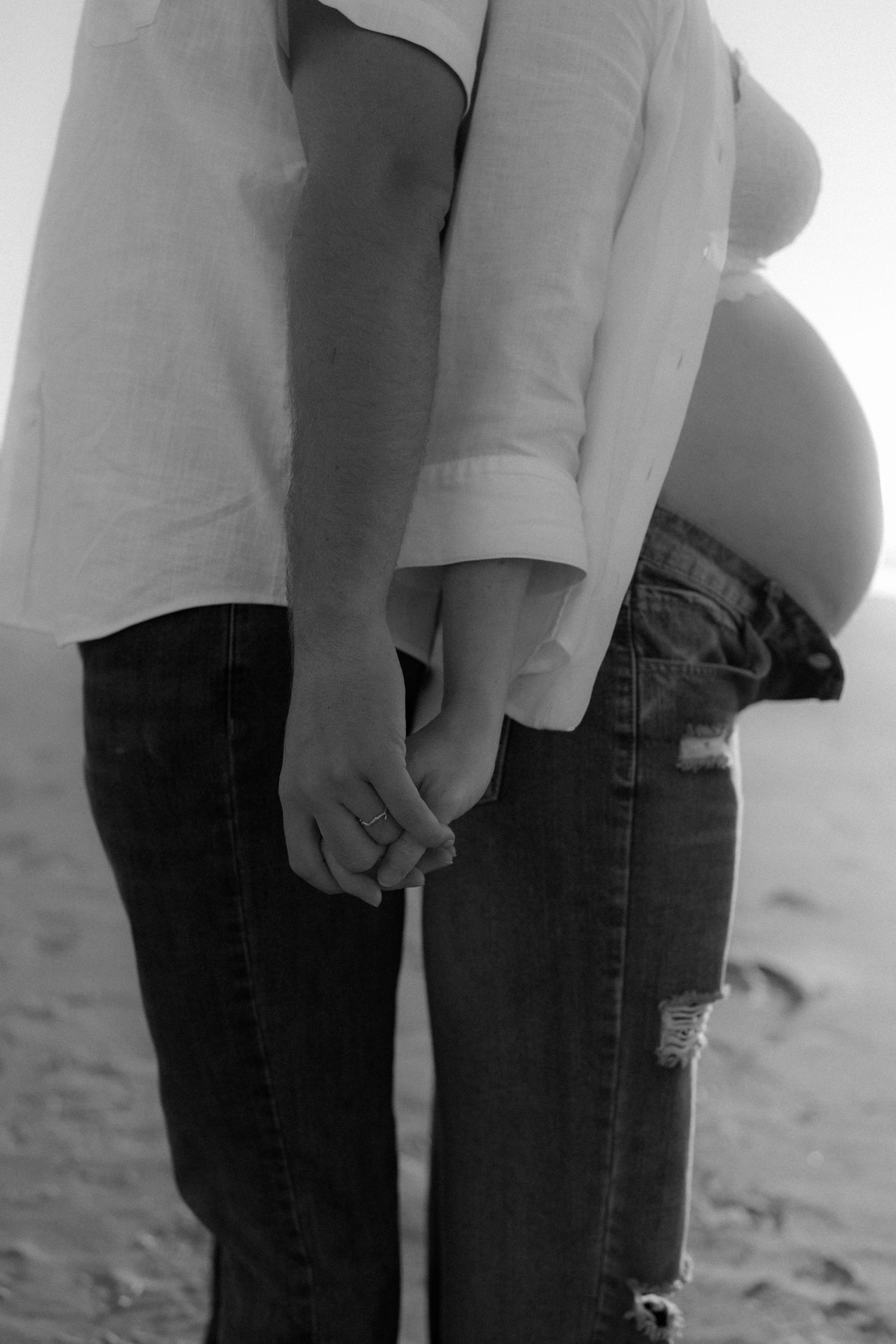 Close-up black and white shot of two people standing together on a beach.