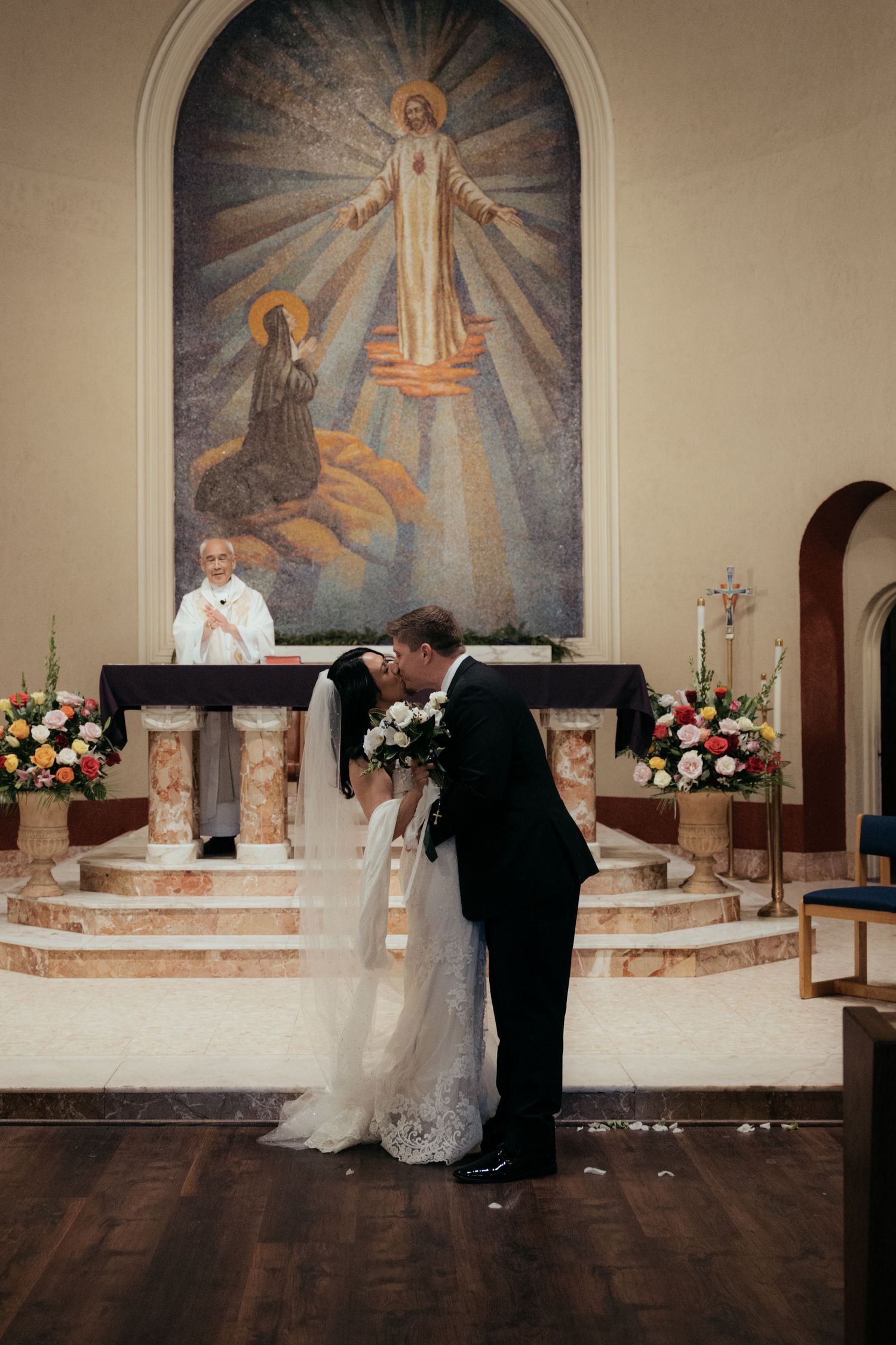 A wedding ceremony taking place at an ornate church altar with religious artwork and floral arrangements.