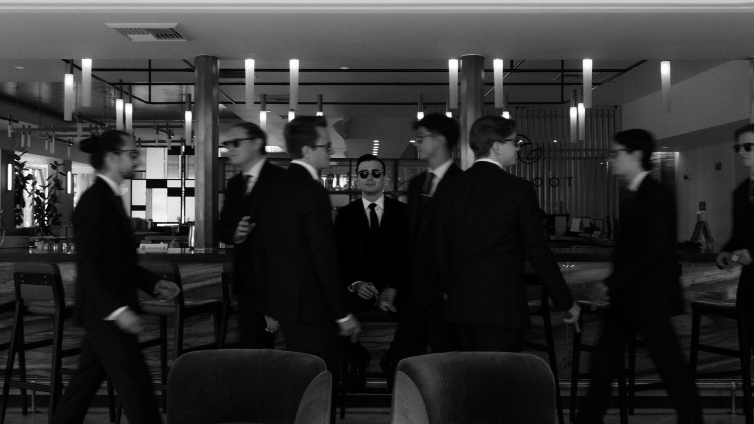 Black and white panoramic view of passengers waiting in an airport terminal security checkpoint area.