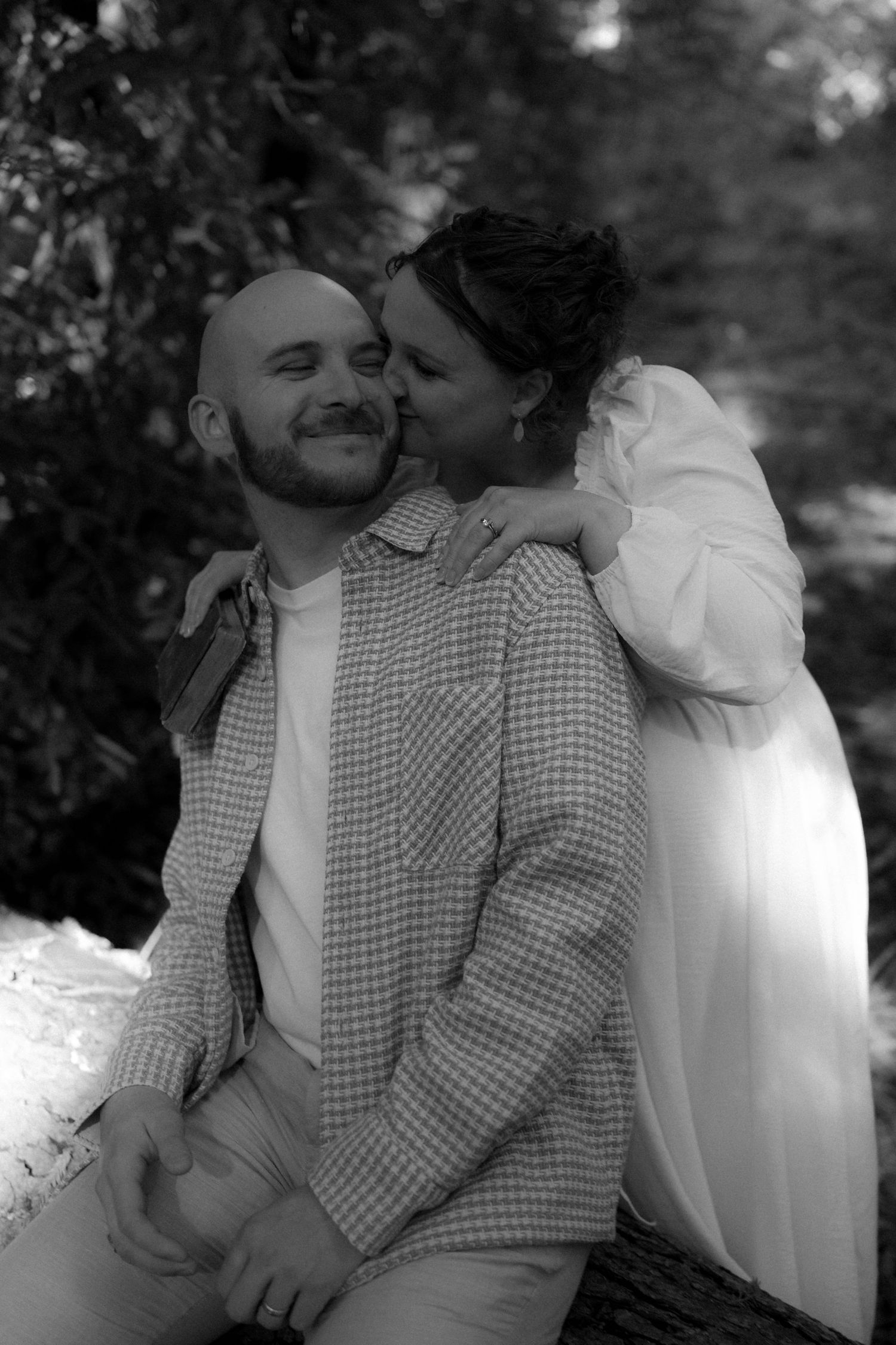 A black and white romantic portrait of a couple sharing an intimate moment outdoors.
