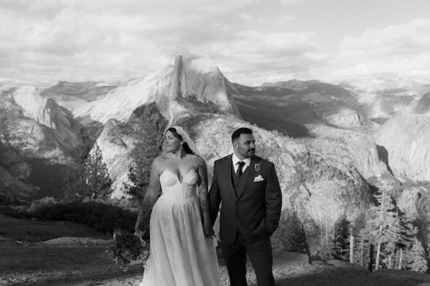 Bride and groom walk hand in hand with Half Dome mountain backdrop at Yosemite.