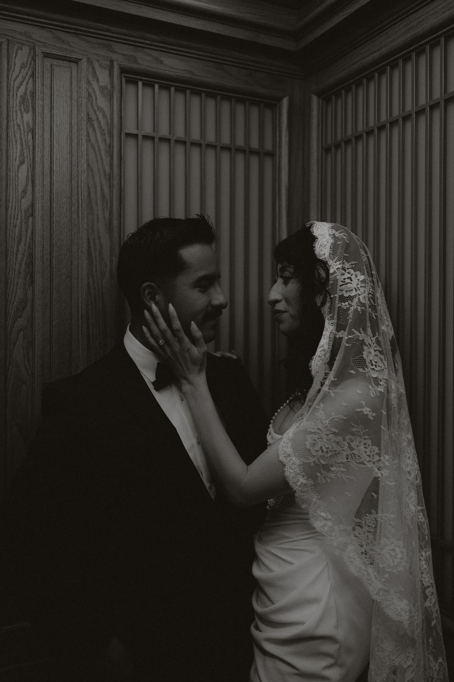 A tender moment between newlyweds in formal attire against a wood-paneled wall.