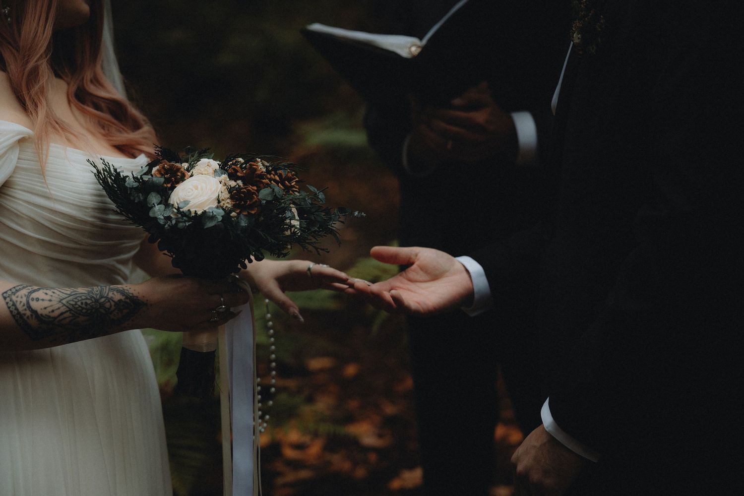 A couple exchanges rings during an intimate outdoor wedding ceremony with autumn leaves on the ground.
