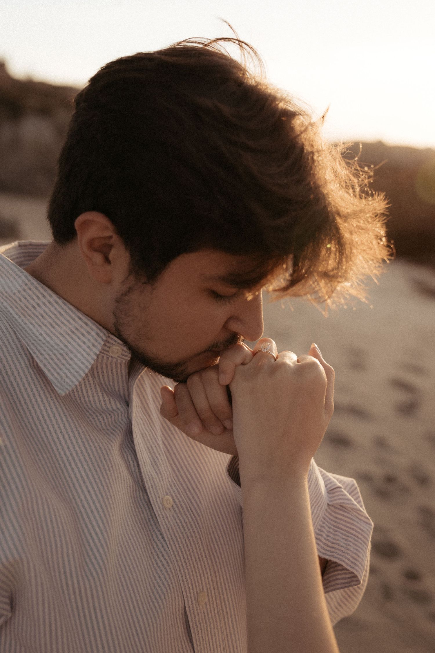 Couple in soft sunlight shares tender moments on a sandy shoreline.