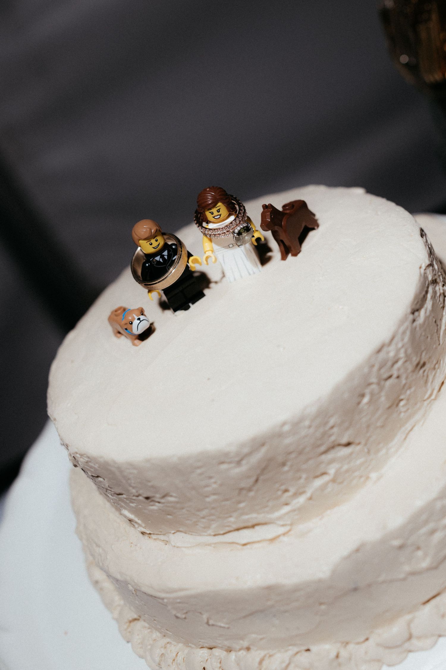 White frosted wedding cake with miniature decorative figures arranged along the curved top edge.