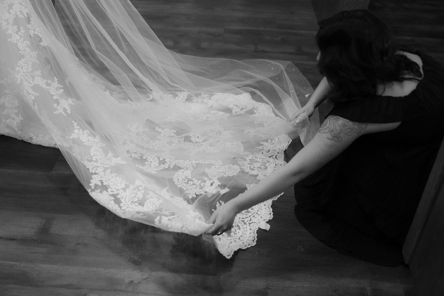 A black and white photo showing the flowing train of a lace wedding dress against a dark background.