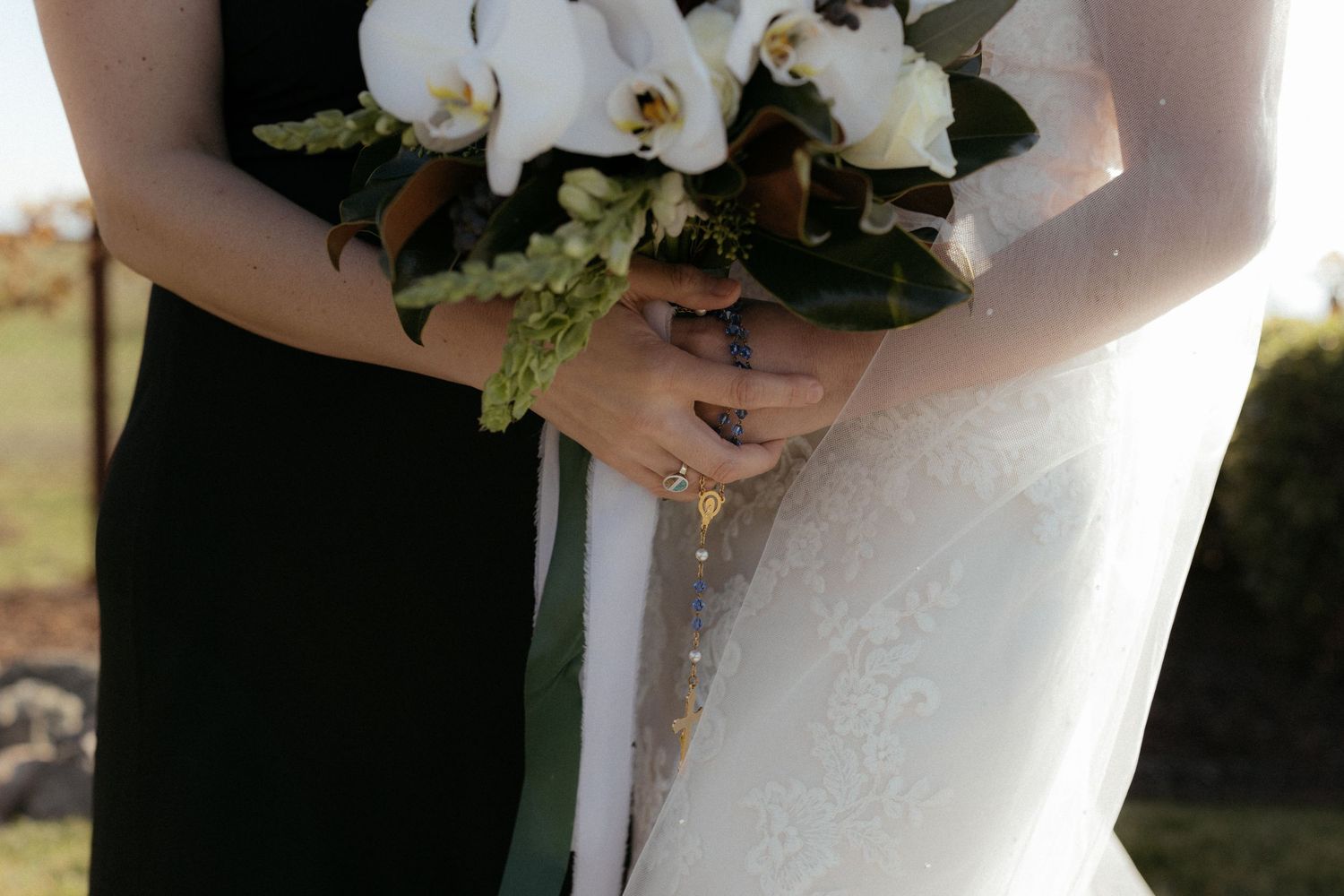 Close-up detail of white wedding bouquet and formal dresses during outdoor ceremony.