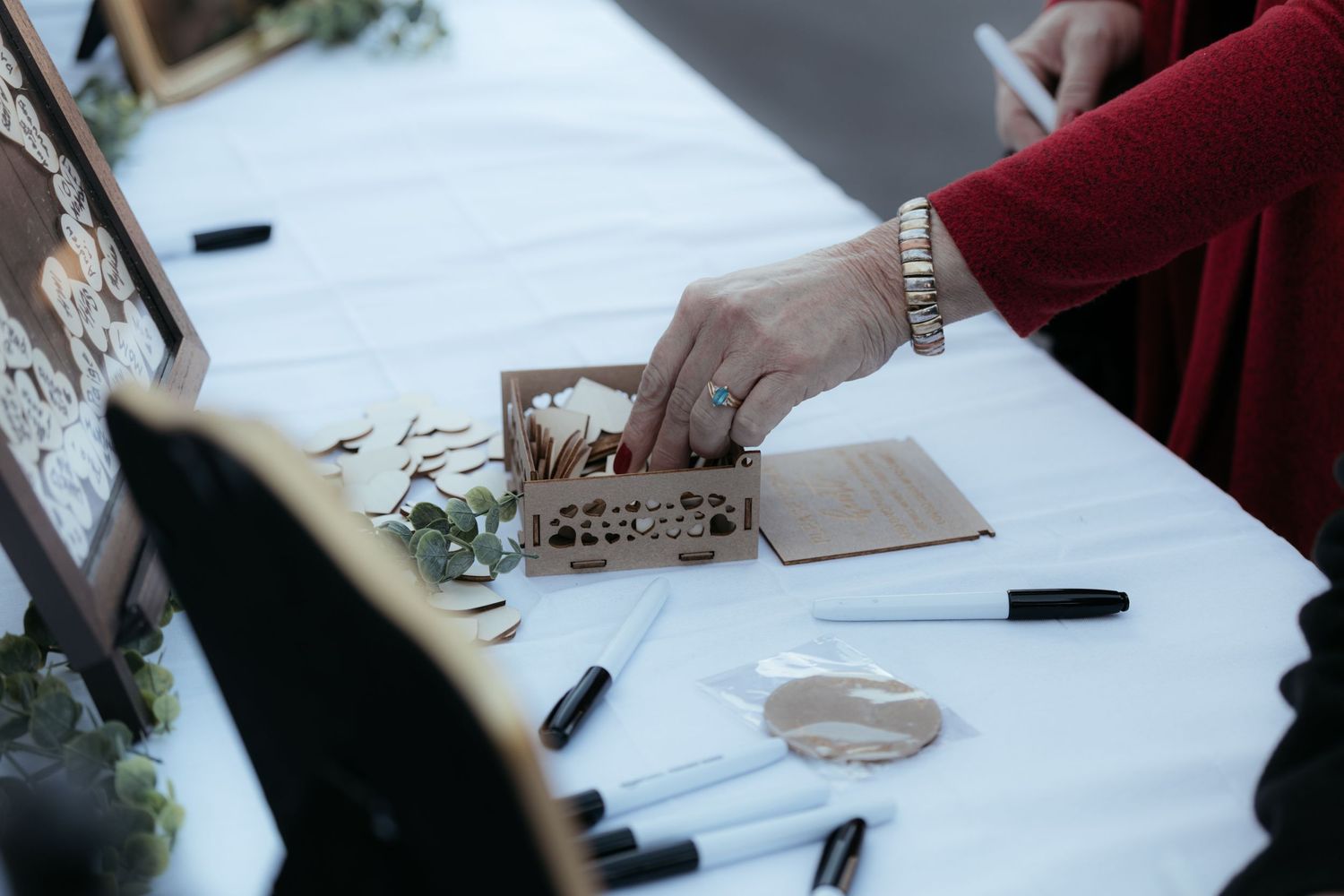 Guests signing a wedding guestbook on a white tablecloth with pens.
