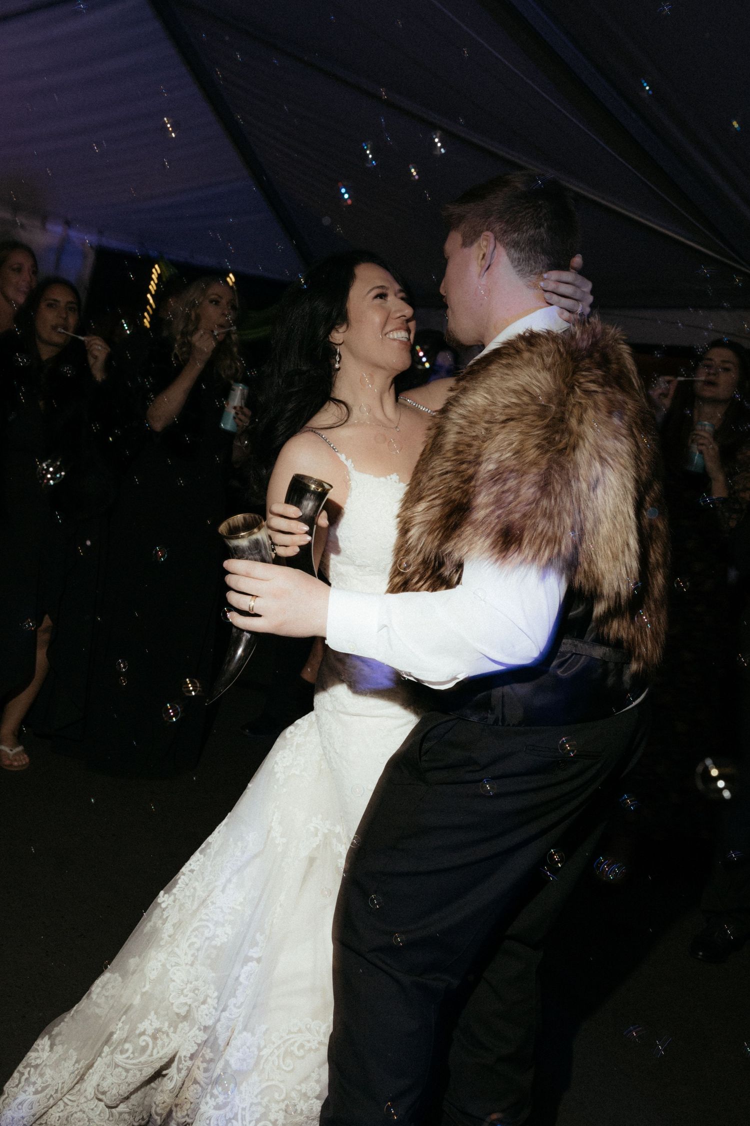 Newlyweds dance together surrounded by guests at their evening reception.