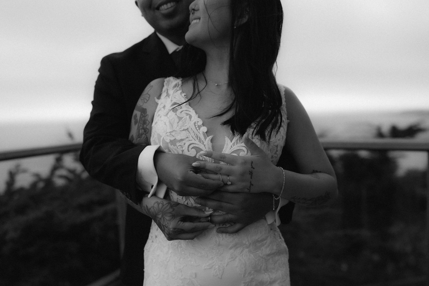 A romantic black and white photo of a couple embracing outdoors, with the bride wearing a lace wedding dress.