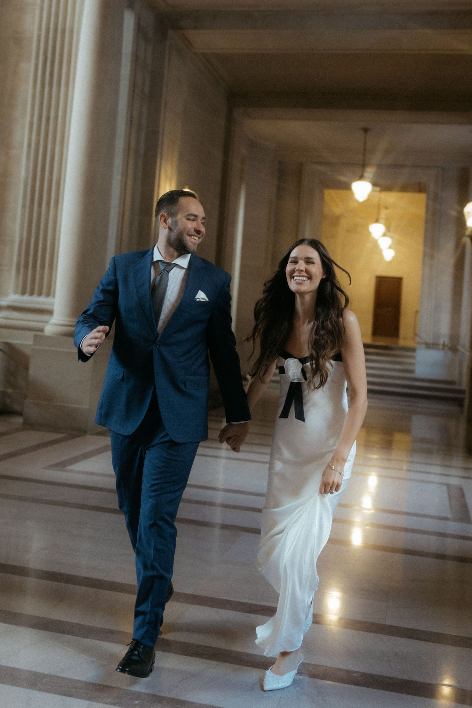 A couple dances playfully in an elegant marble hallway with classical columns and warm lighting.