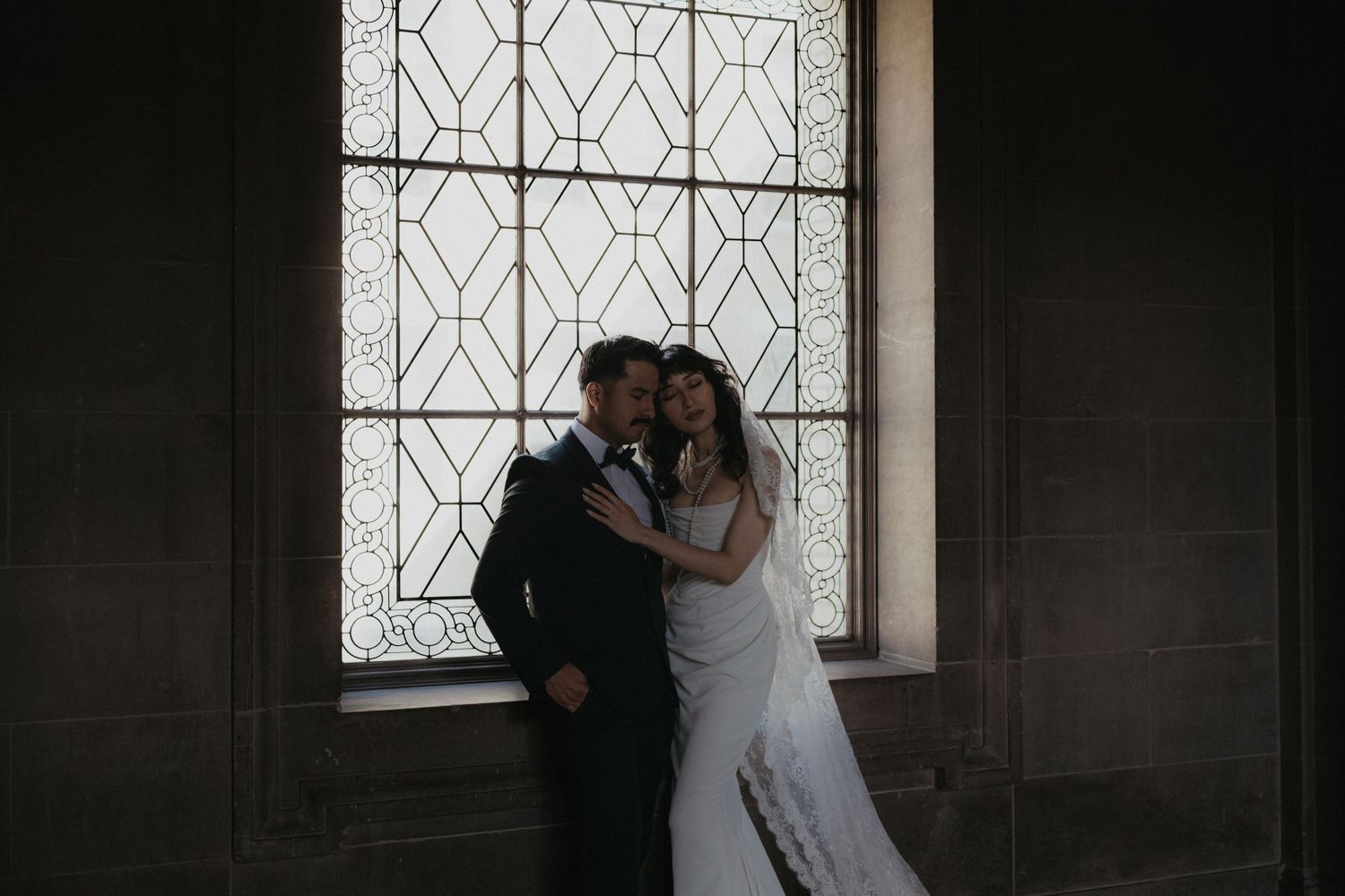 A tender moment between newlyweds sharing an embrace by a patterned window.