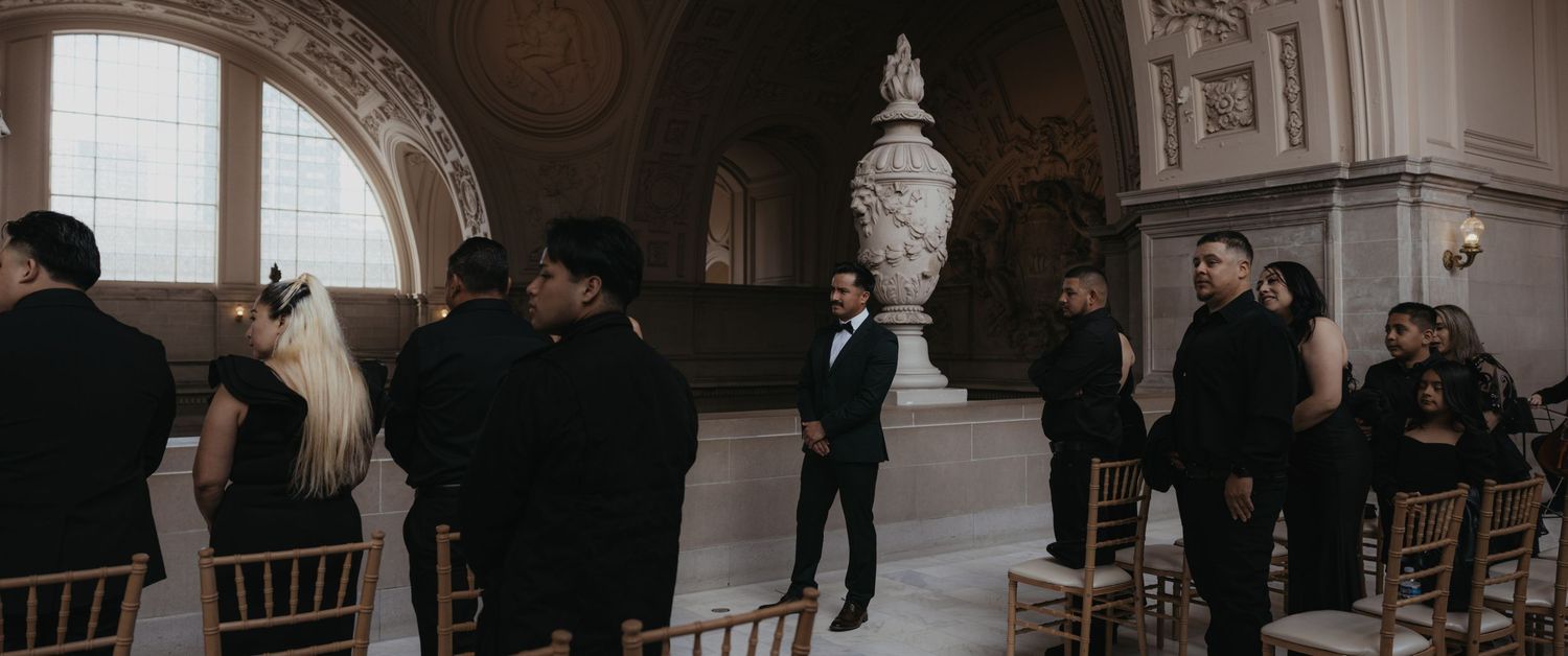 Wedding party walking through an elegant hallway with arched ceilings and hanging pendant lights.
