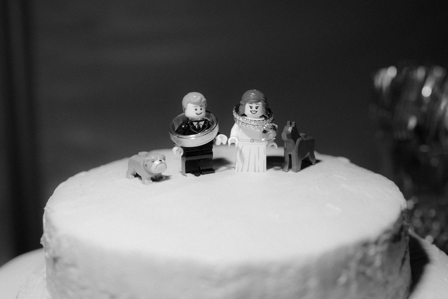 Wedding cake with white frosting and small decorative elements displayed against dark background.