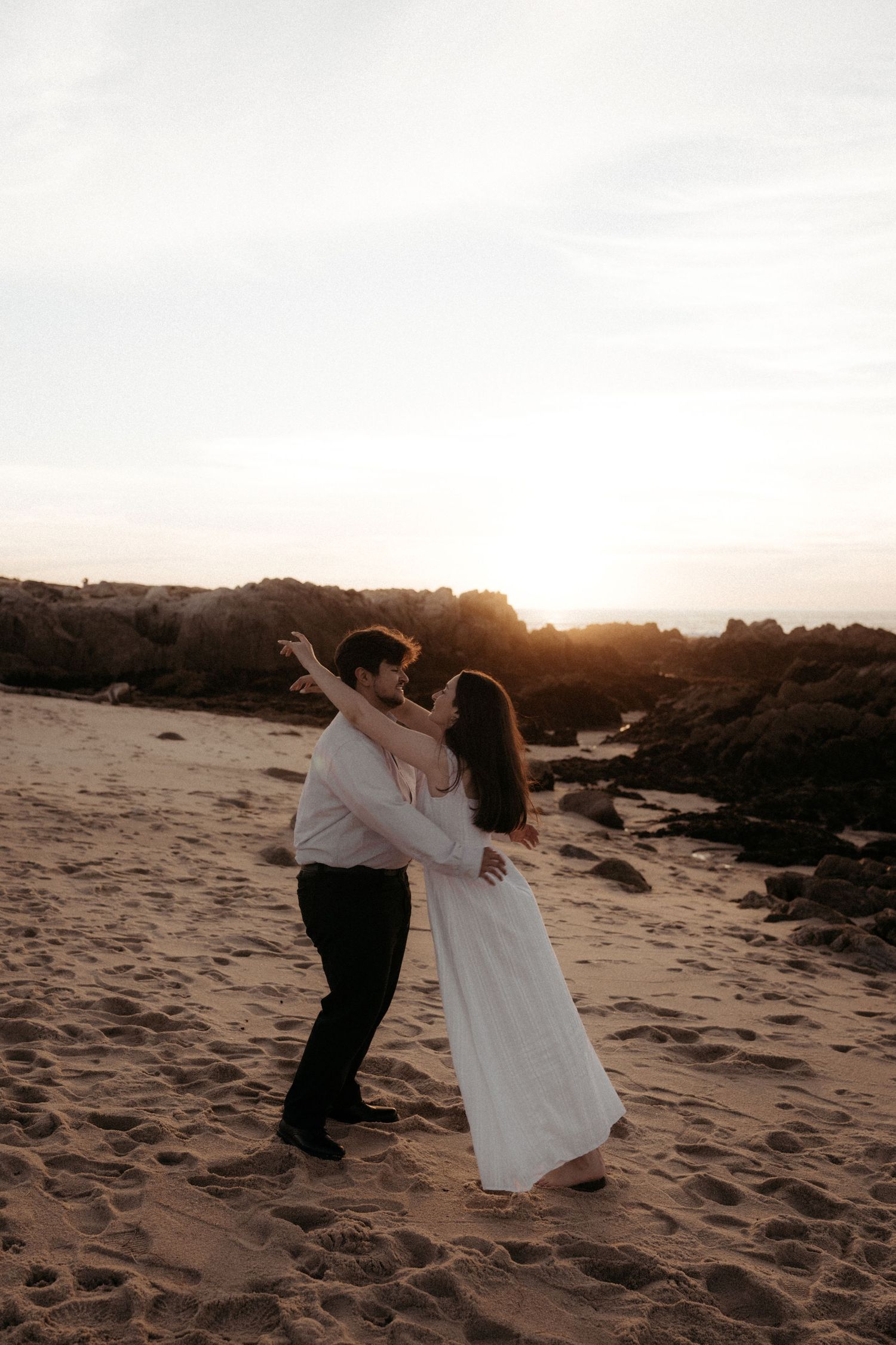 A romantic beach photoshoot at sunset shows a couple dancing and dipping in the golden light on sandy dunes.
