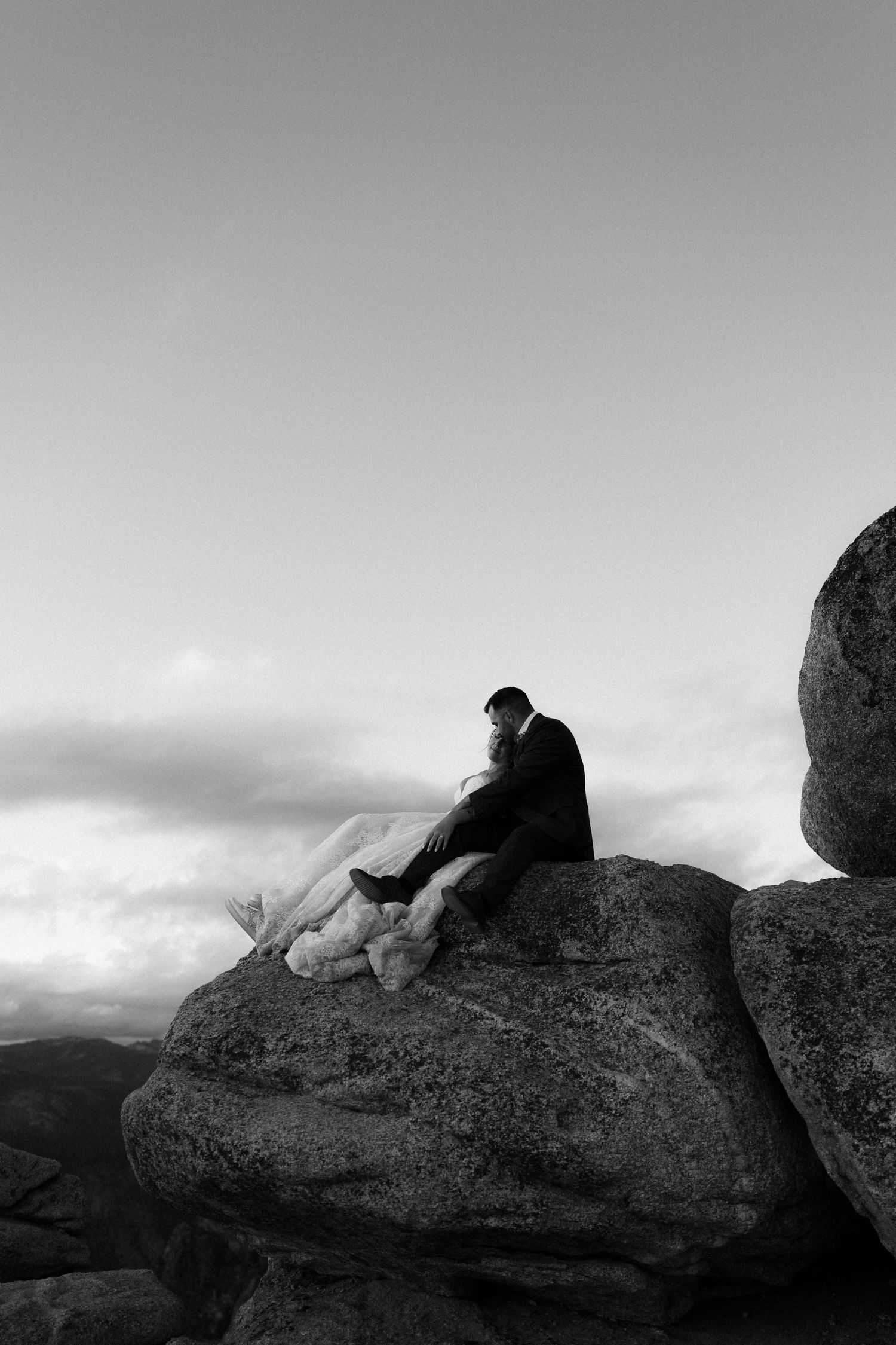 Black and white photo of a bride and groom sitting together on a rocky mountain summit.