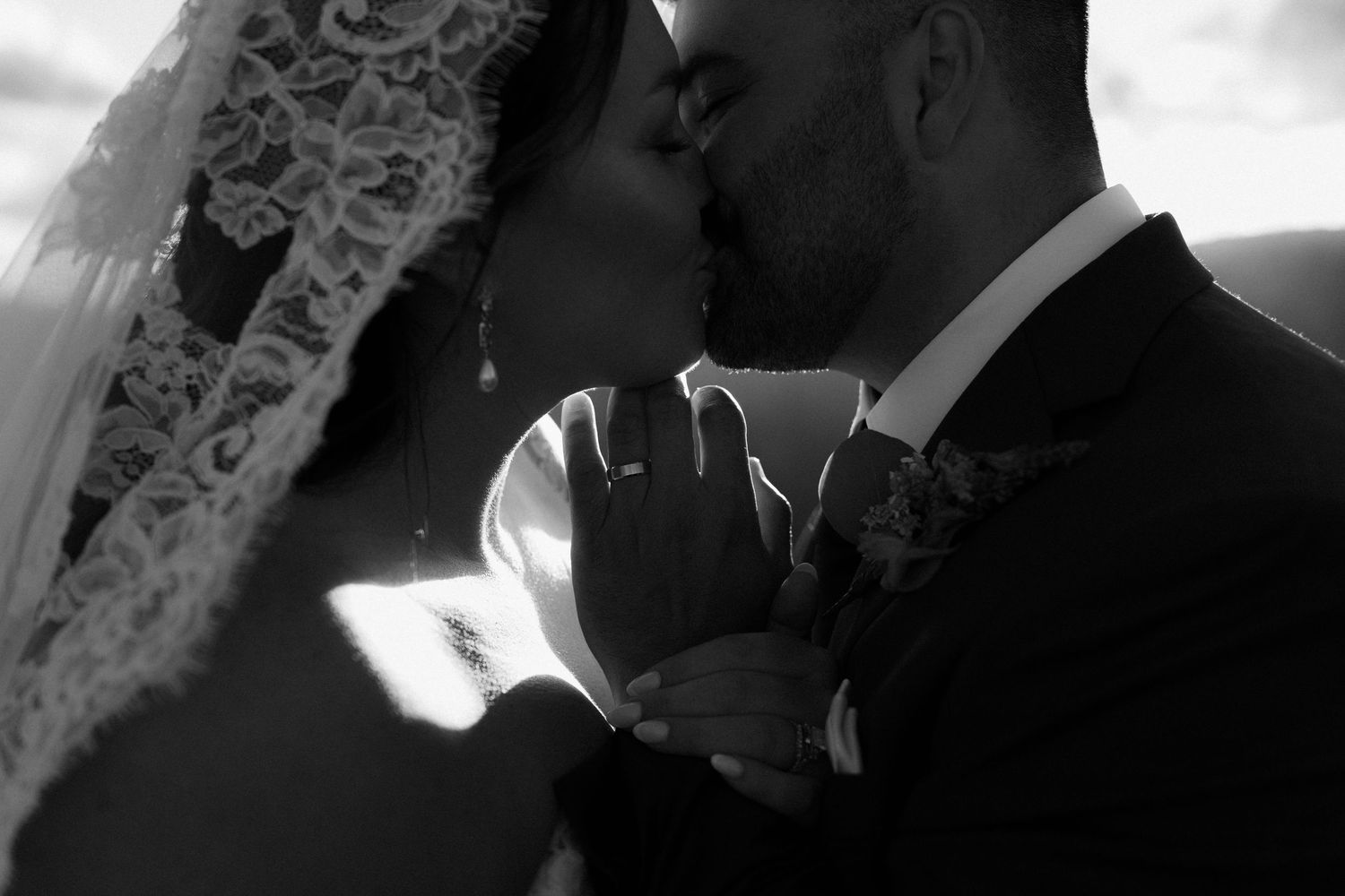Black and white wedding photo of bride and groom sharing a romantic kiss, bride wearing lace veil.