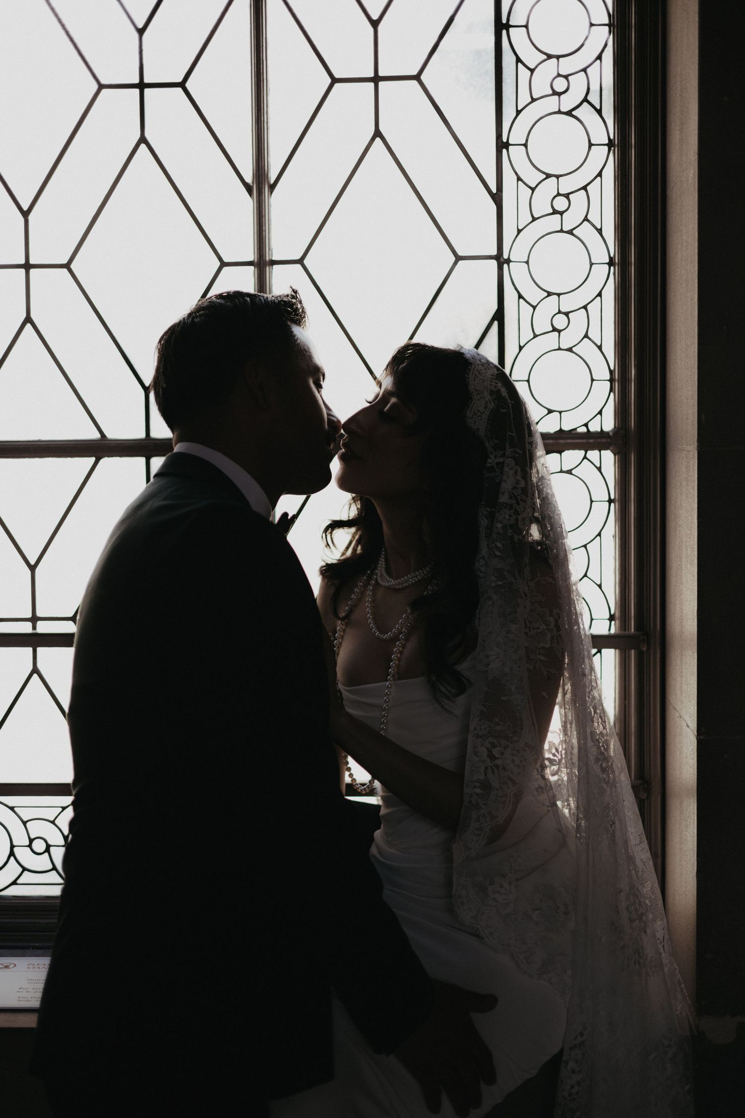 Silhouette of bride and groom sharing a tender moment in front of an ornate stained glass window.