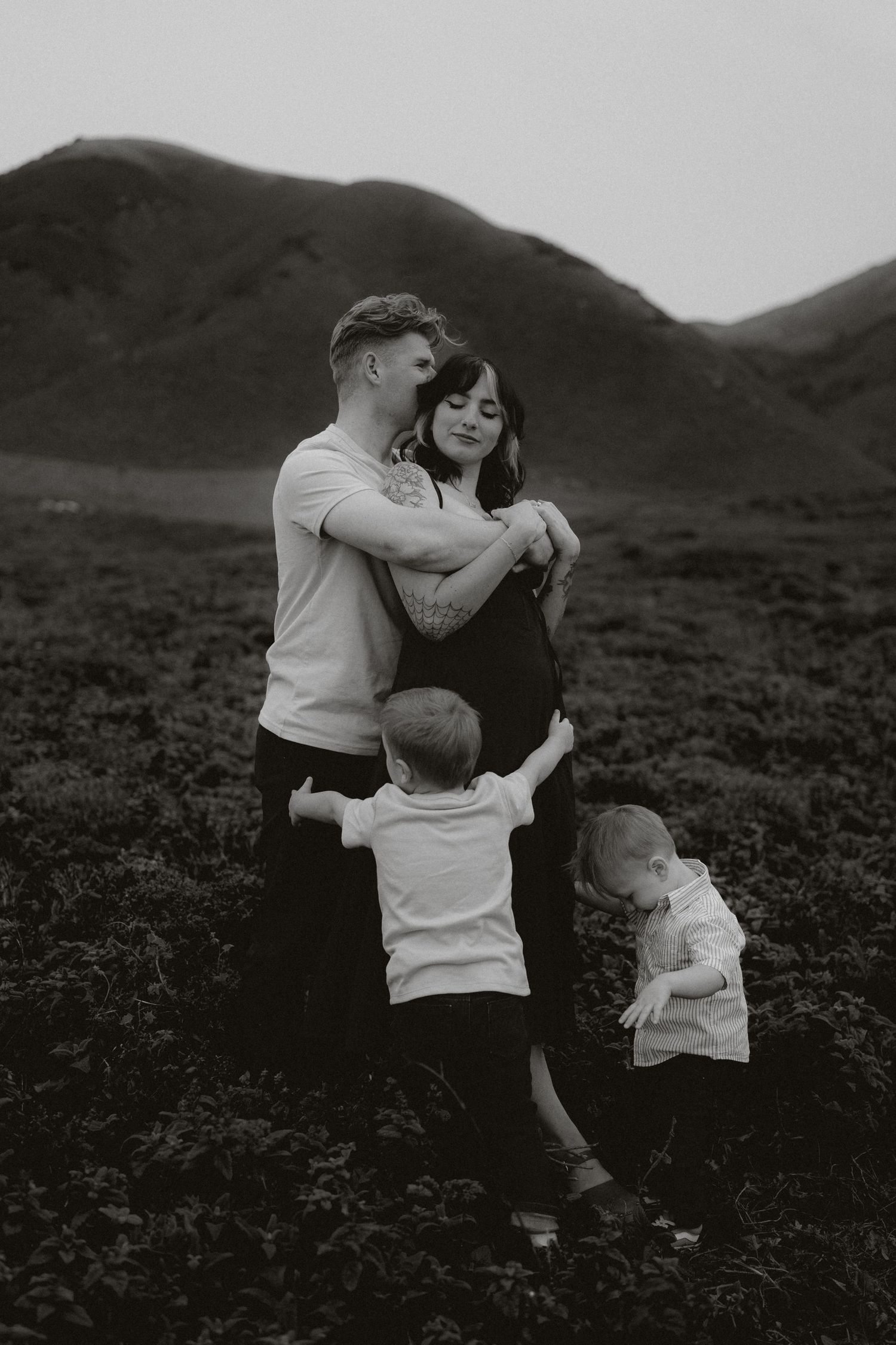 Black and white photograph showing intimate family moments against a mountainous landscape.