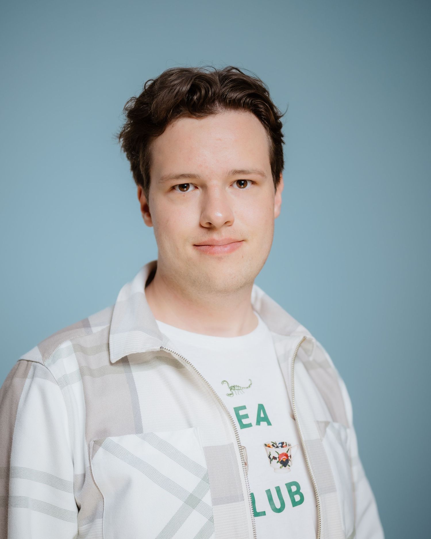 Portrait of a person in casual attire smiling against a blue studio backdrop.