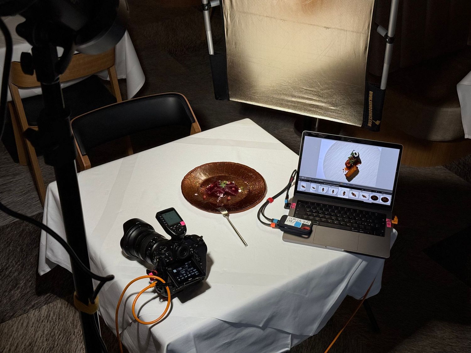 Photography setup with camera, laptop and bowl on white tablecloth.