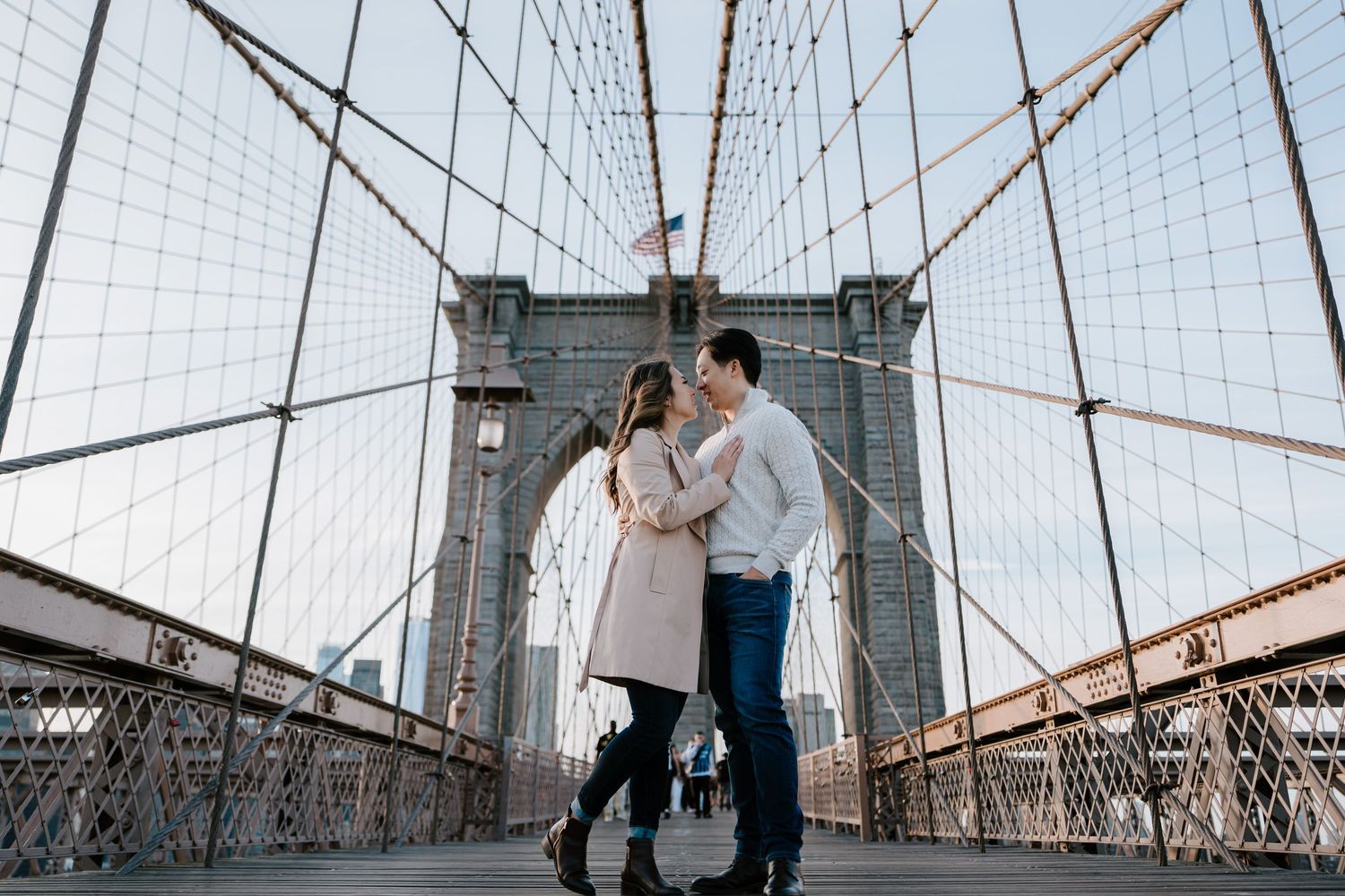 Couple embracing on Brooklyn Bridge walkway with iconic suspension cables and stone tower in New York City.