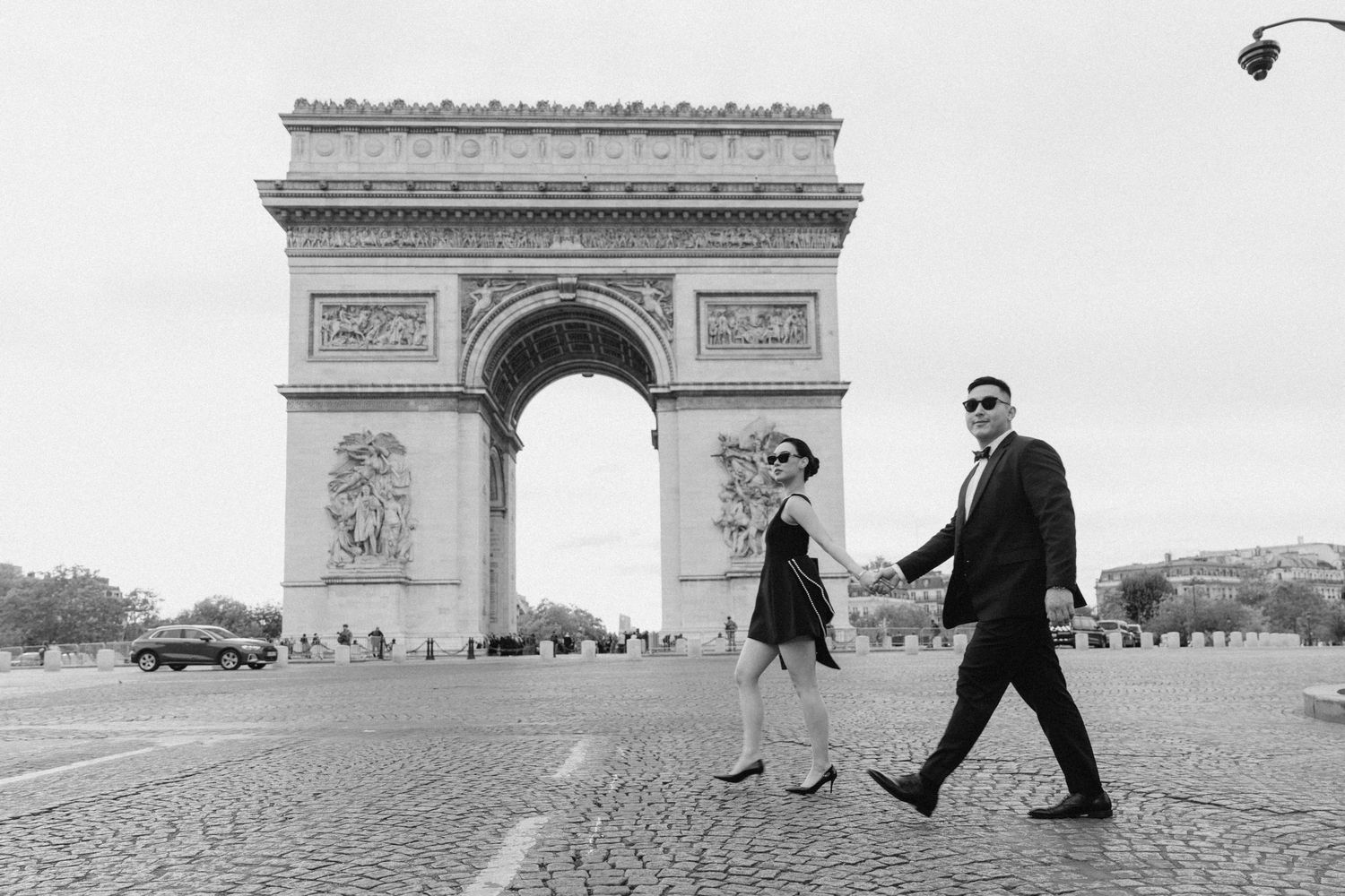 Couple holding hands walking in front of the Arc de Triomphe in Paris, black and white photo.