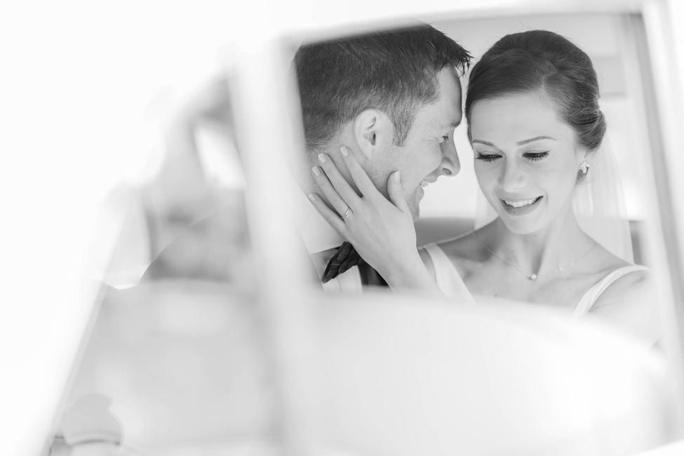 Black and white wedding photo of a couple sharing a romantic moment, smiling and touching foreheads tenderly.