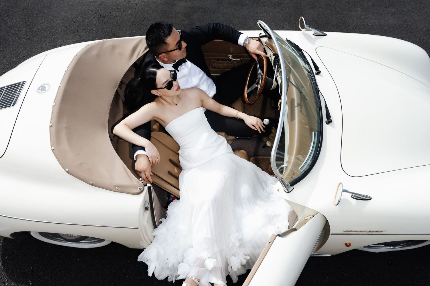 Bride and groom sharing a romantic kiss in a classic white vintage convertible car on their wedding day.