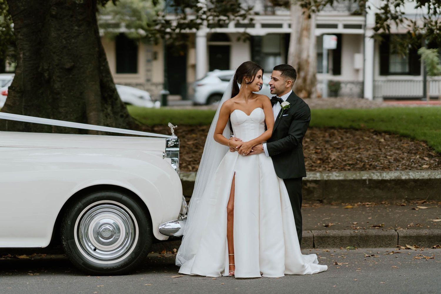 Bride and groom posing beside a classic white vintage car on their wedding day.