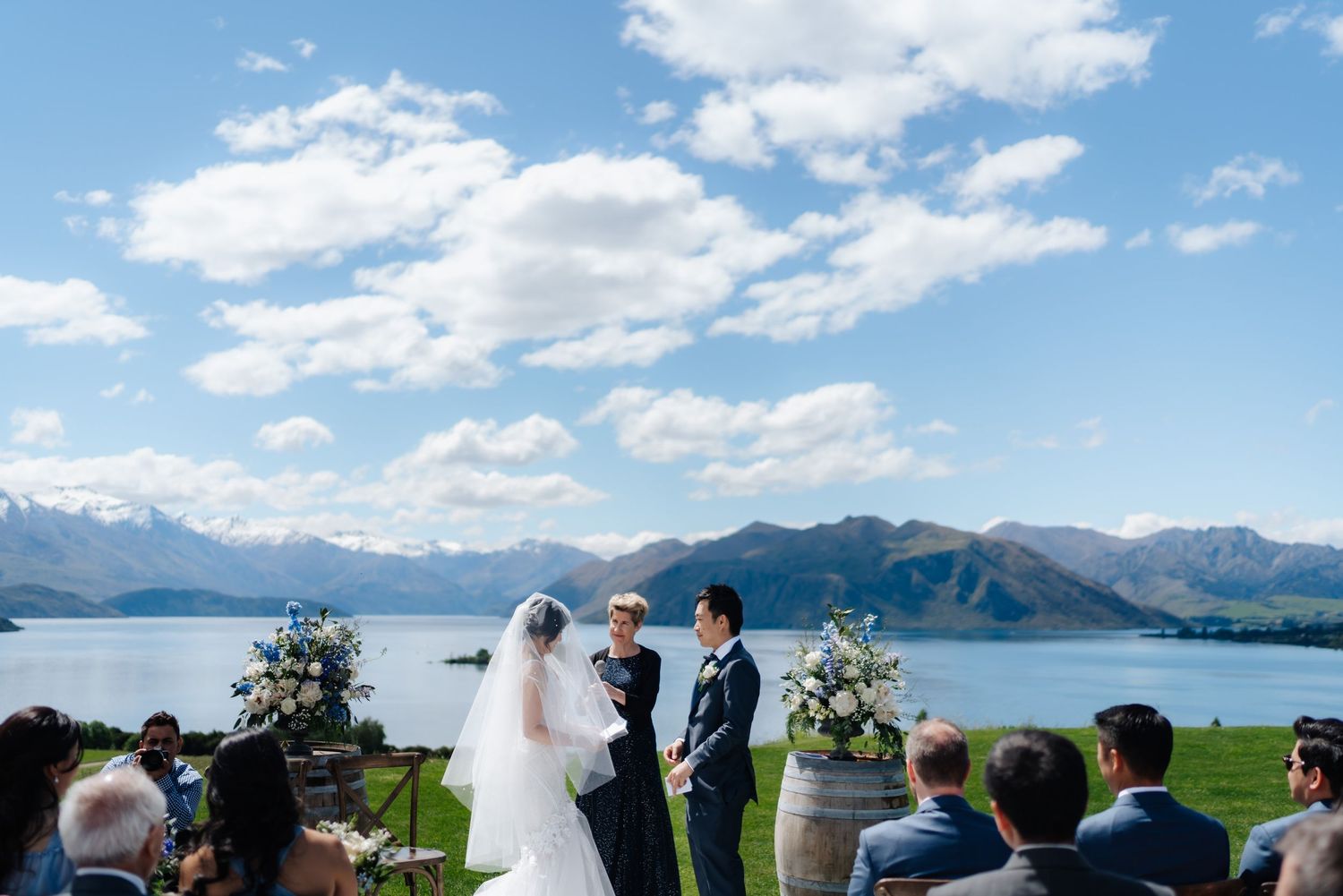 Outdoor wedding ceremony by a scenic lake with mountain backdrop under blue skies in New Zealand.