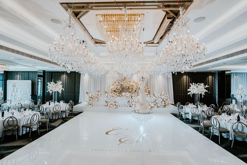 Elegant white wedding reception hall with opulent crystal chandeliers and luxurious table settings for celebration.