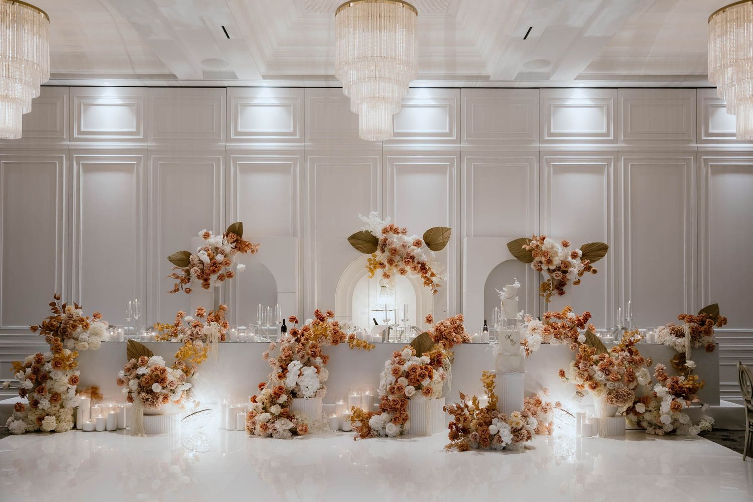 Elegant white wedding reception venue with romantic floral arrangements and warm lighting against paneled walls.