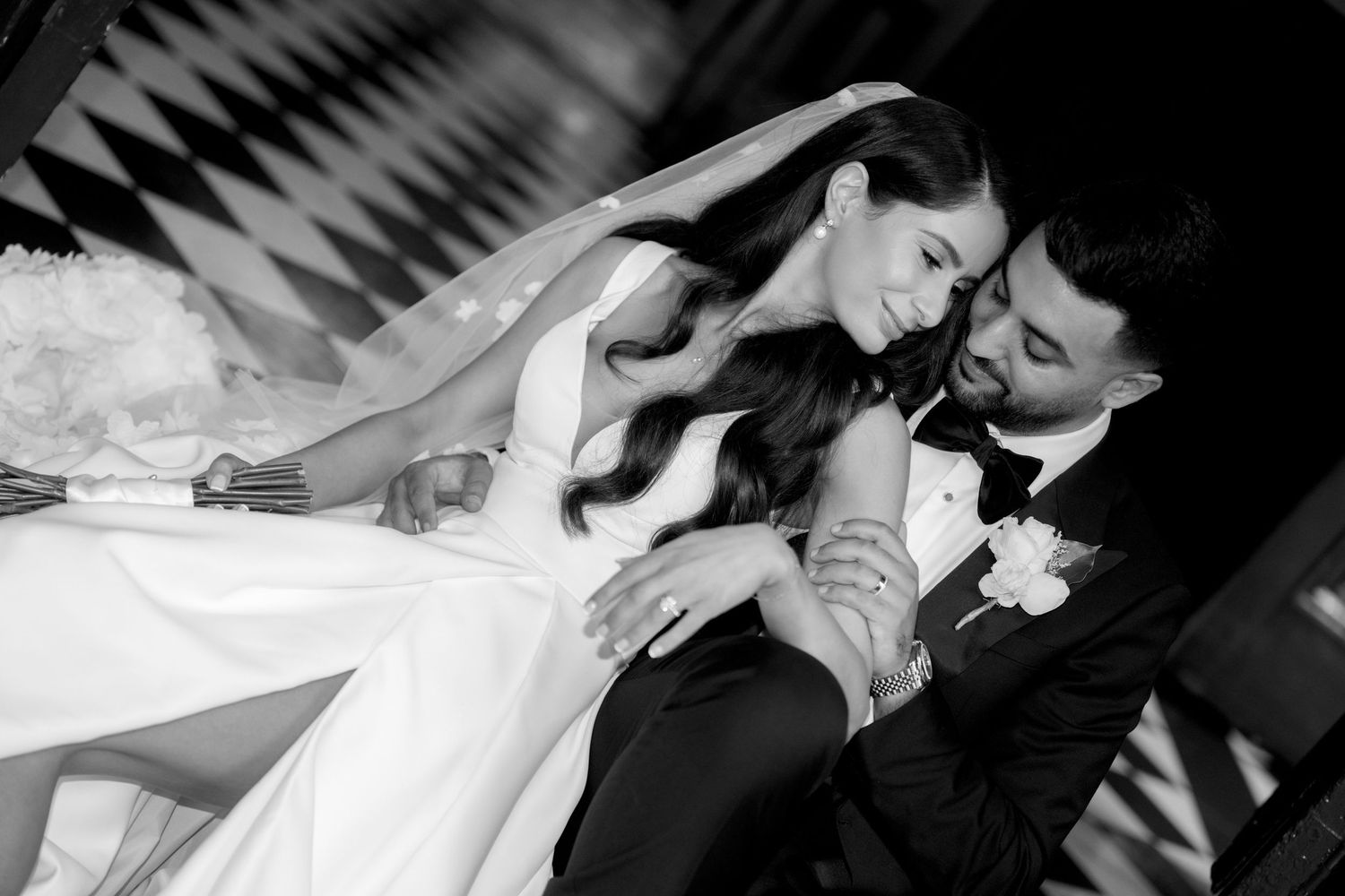 Black and white wedding photo of bride and groom sharing an intimate moment, bride in veil and gown, groom in tuxedo.