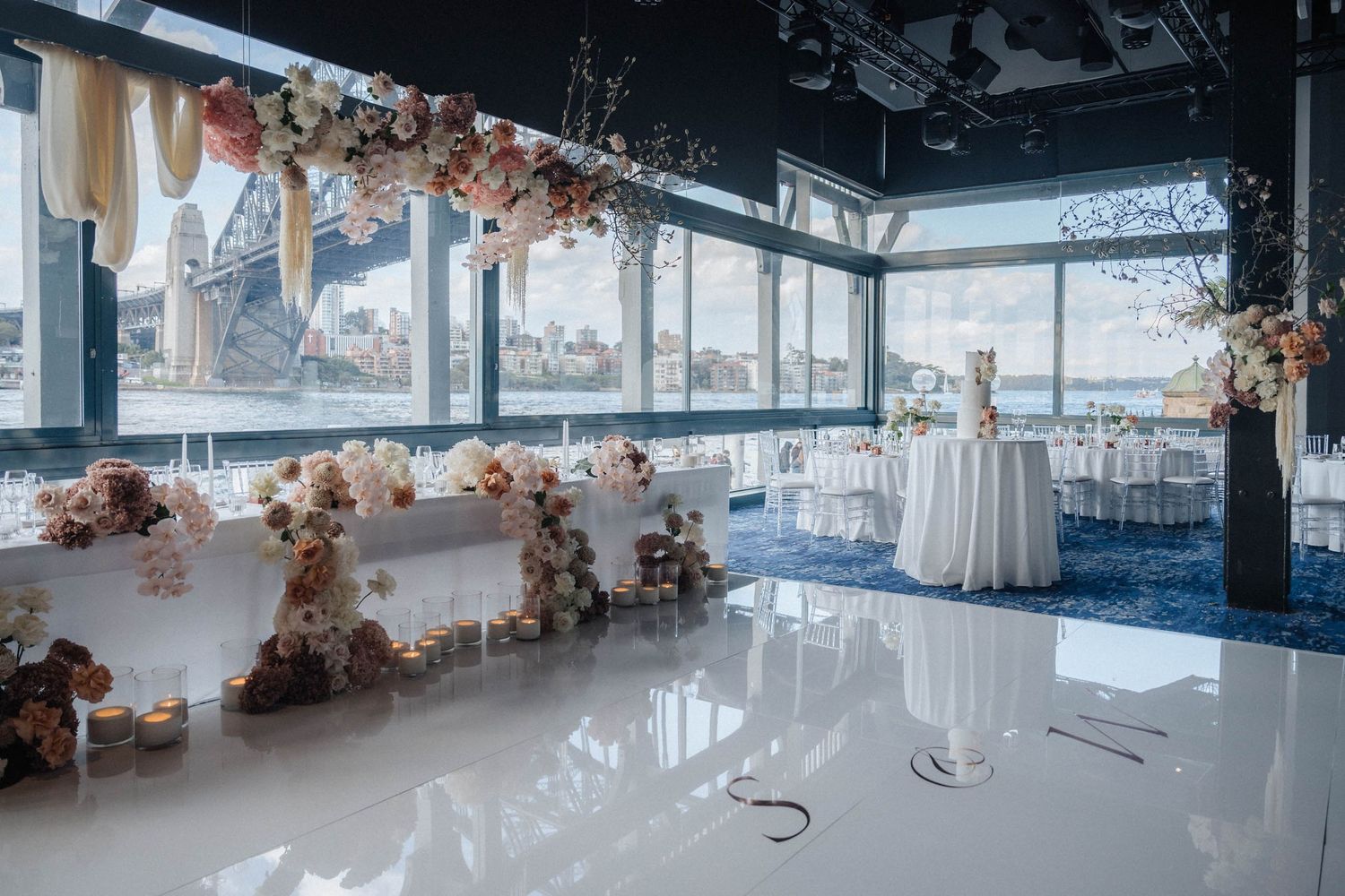 Modern event venue interior with white curtains, chandeliers, and floor to ceiling windows offering panoramic views.