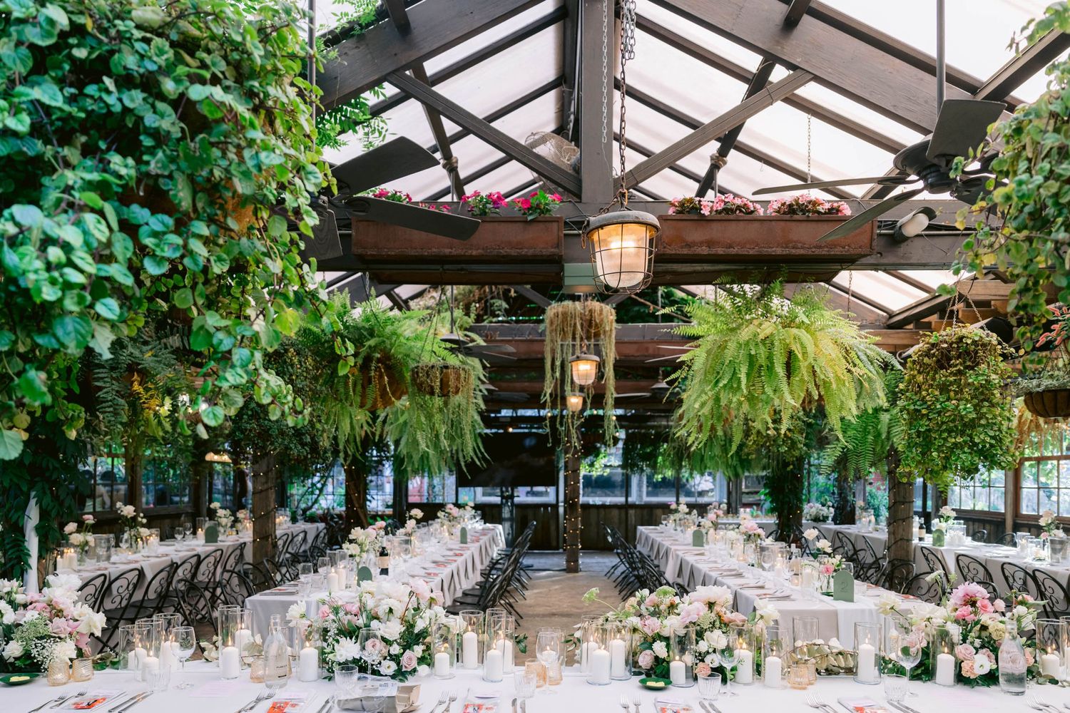 Table settings under a wooden pergola create an elegant outdoor dining atmosphere with lush greenery and hanging lanterns.