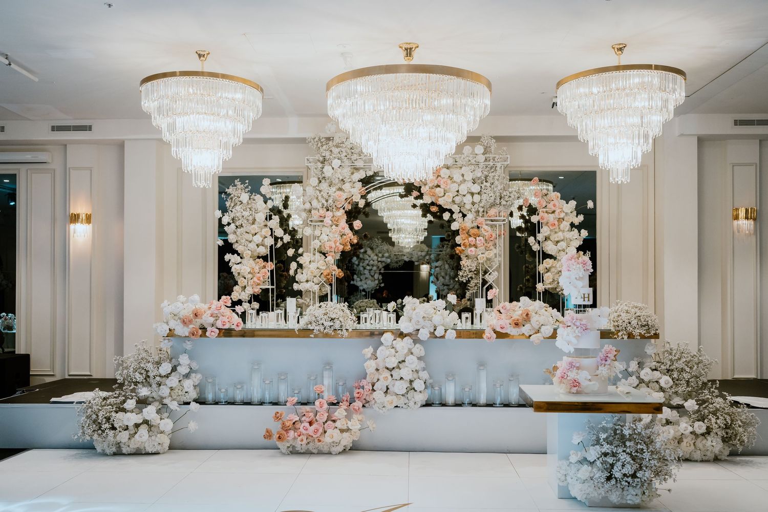 Elegant wedding reception venue with crystal chandeliers and cascading white orchid arrangements adorning the head table decor.