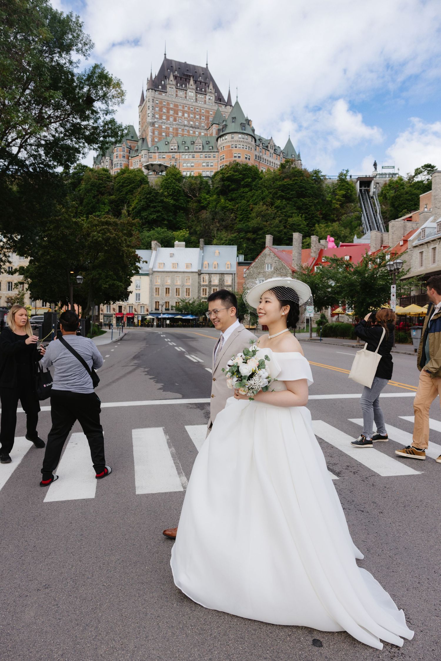 Newlywed couple in wedding attire crossing street near Chateau Frontenac in Old Quebec City, Canada.