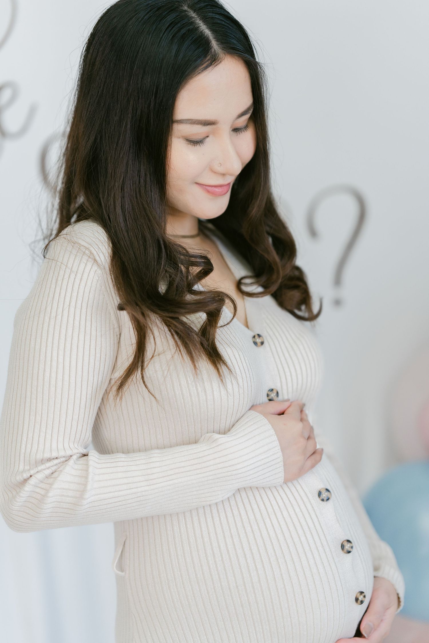 Close-up of a glowing pregnant woman in a studio setting, wearing a soft, elegant gown and gently holding her belly