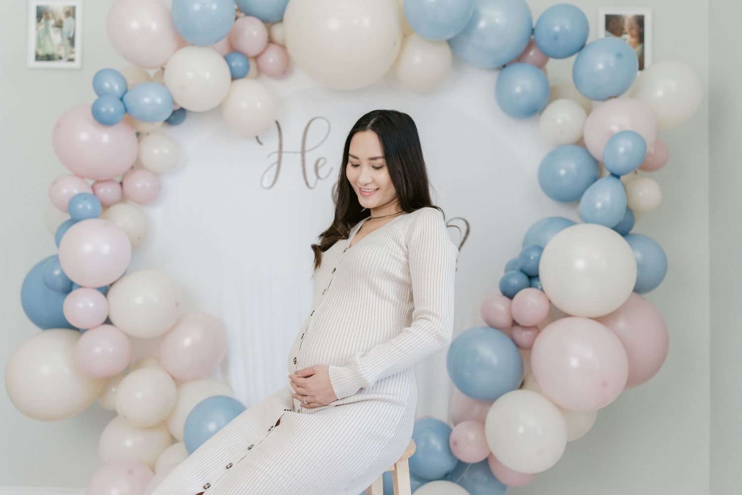 Close-up of a glowing pregnant woman in a studio setting, wearing a soft, elegant gown and gently holding her belly