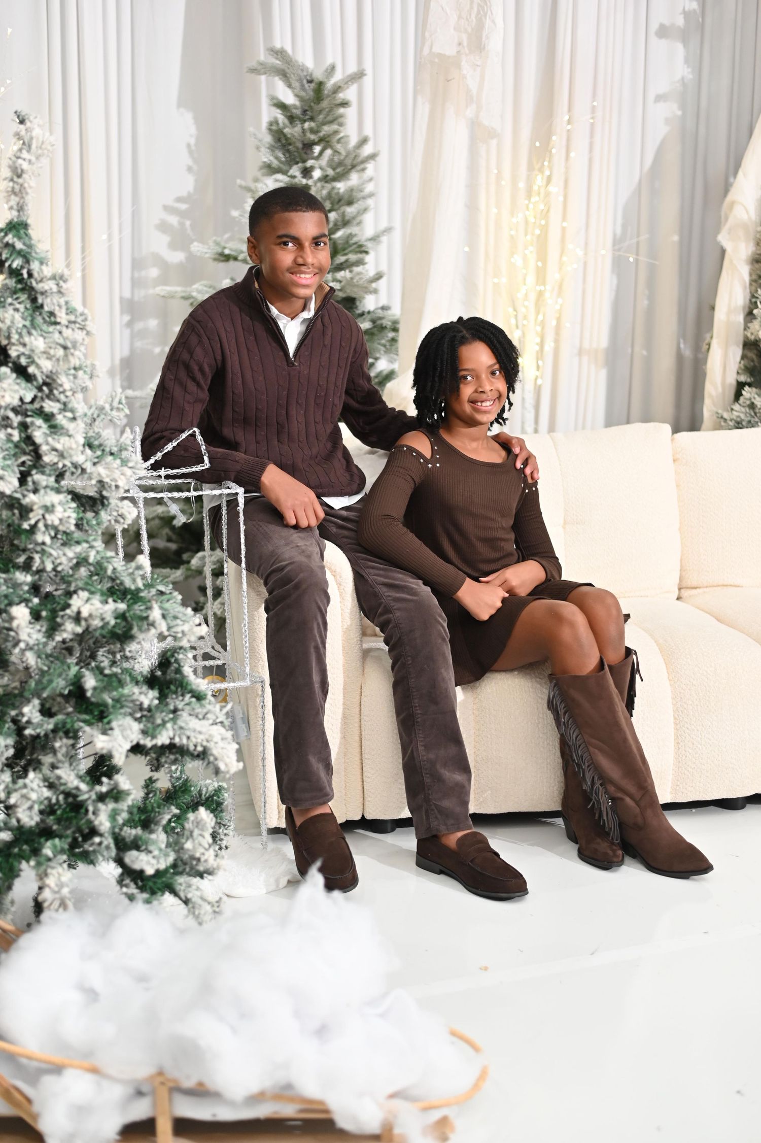 A couple sits together on a white couch with snowy Christmas trees and decorations creating a cozy winter scene.