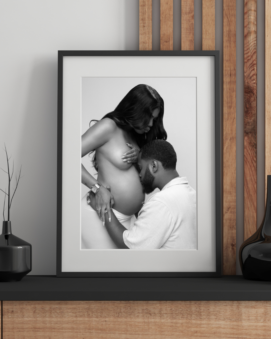 Black and white photos of tender moments displayed on wooden shelves with alternating frames and decor pieces.